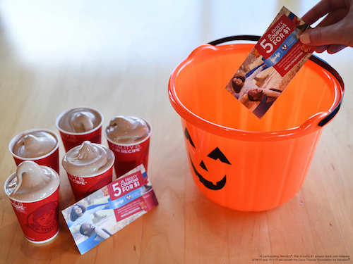 An orange pumpkin bucket with Wendy\'s Frostys and Frosty coupons beside it.